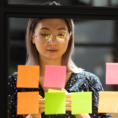 Young woman planning a corporate awards event with post it notes stuck on glass window.